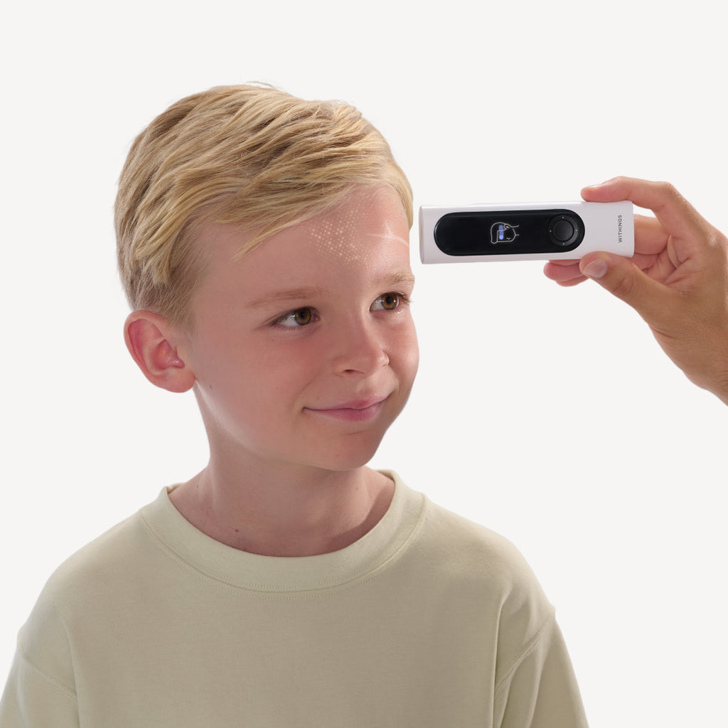 BeamO — Beam-O — Erwachsene Hand hält das Gerät, um die Stirntemperatur eines lächelnden blonden Kindes zu messen, weißer Hintergrund — Stirnscan, Kind, Erwachsene Hand, Nahaufnahme