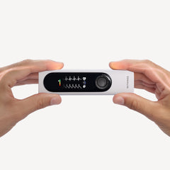 Withings BeamO — Beam-O — Gerät wird horizontal mit beiden Händen gehalten, EKG-Bildschirm leuchtet, weißer Hintergrund, stilisiertes Licht auf den Fingern — zwei Hände, aktiver Bildschirm, handgeführt