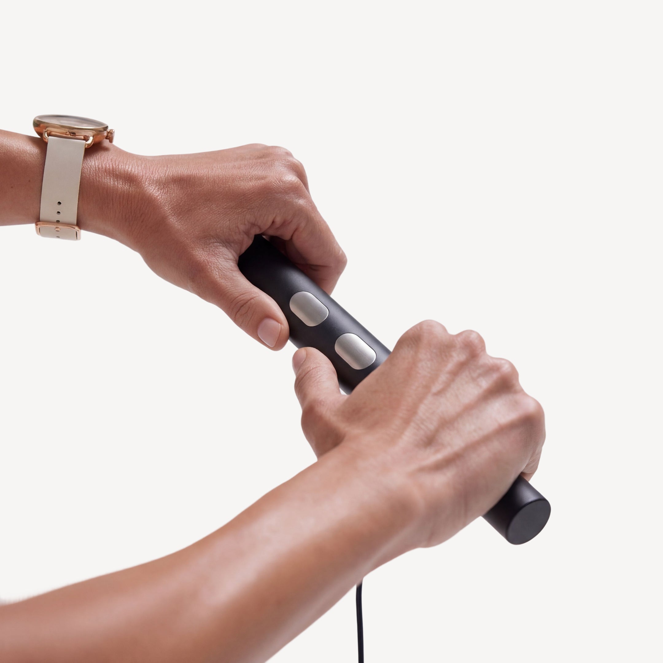 BodyFit — Black — Two hands gripping the black cylindrical device with silver buttons, cable attached, clean white background — close-up, two hands, cable