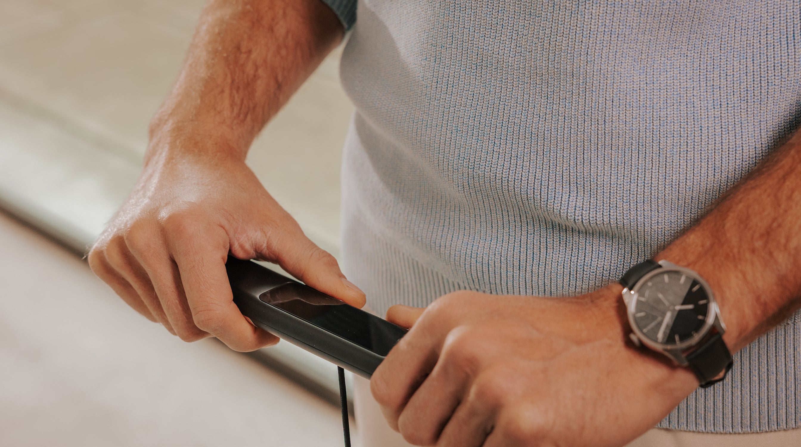 Withings BodyScan 2 — Black — Man's hand pressing the handle sensor, analog watch on wrist, light grey knit sweater, close-up grip — close-up, handle, sensor, hand