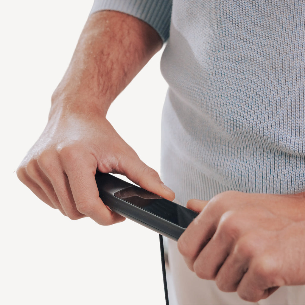 BodyScan 2 — Black — Hands gripping the device handle, close-up view on white background, light grey knit sweater — close-up, hands, handle, neutral background