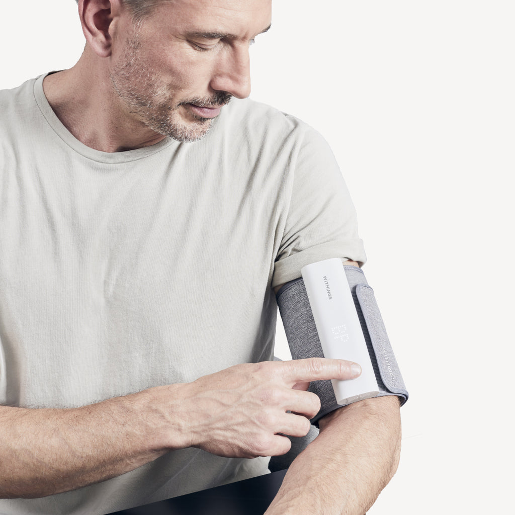 Withings BPM Connect — Verbunden — Mann drückt auf den Knopf einer Manschette am linken Oberarm, sauberer weißer Hintergrund — Manschette, Blutdruck, Arm, Nahaufnahme