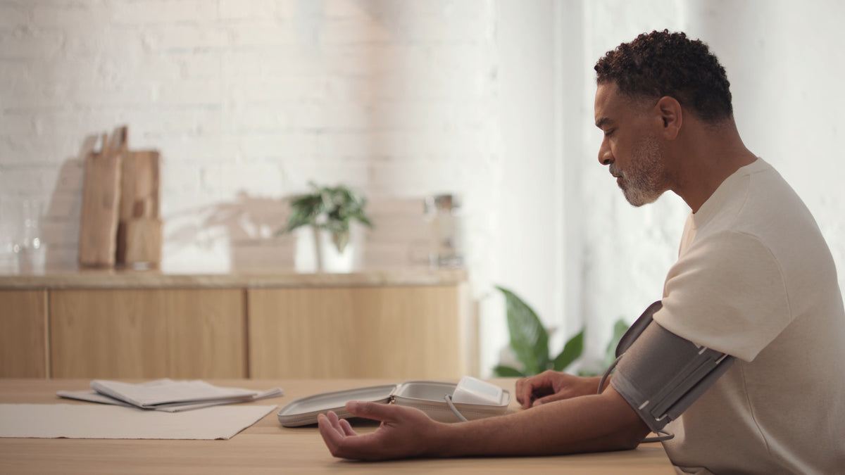 Withings BPM Vision — Blood pressure monitor cuff — Man taking blood pressure reading at kitchen table, natural light, side profile view — side view, kitchen, arm cuff, self-monitoring