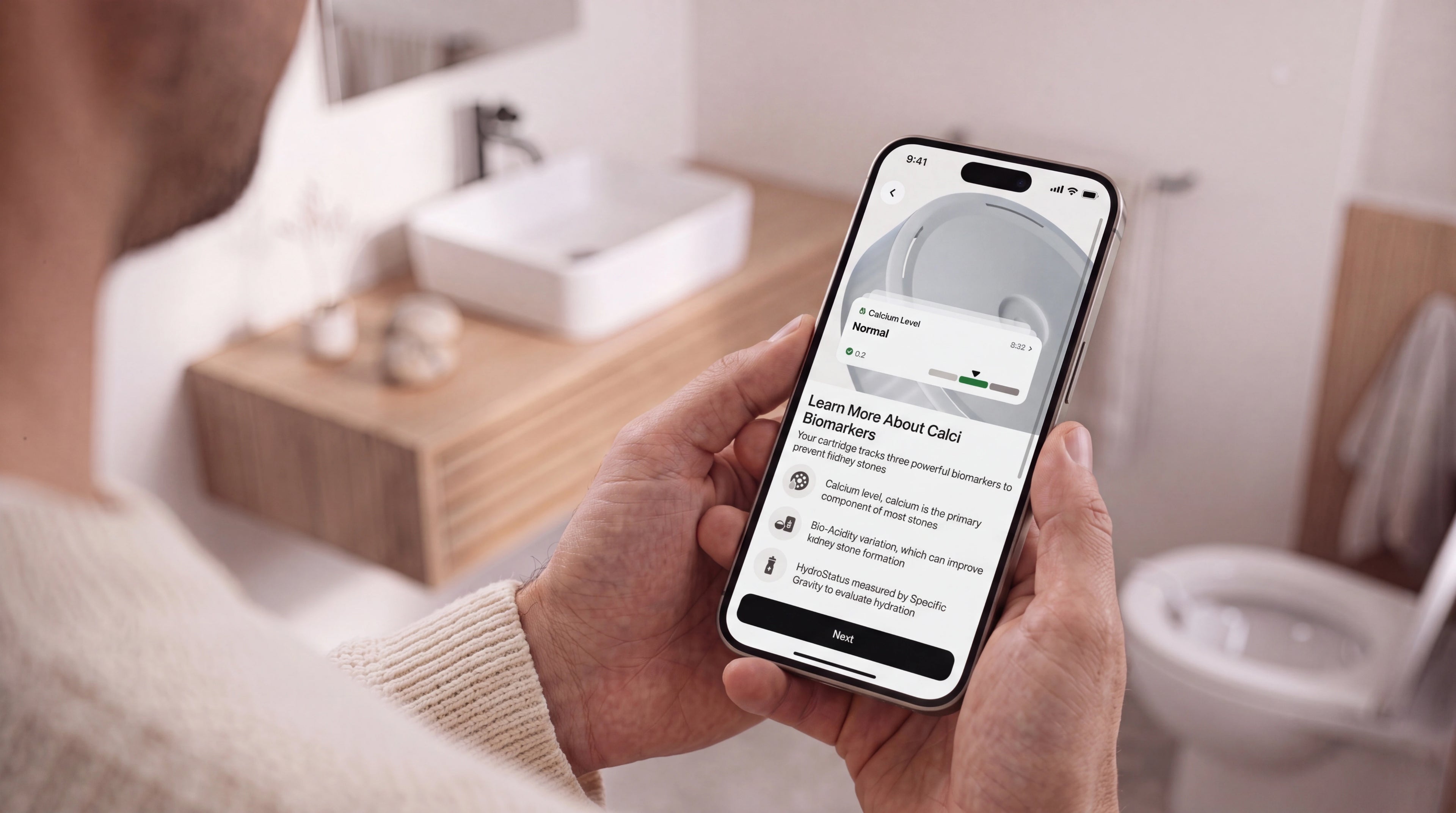 Withings U-Scan Calci — Calci Variant — Man holding iPhone displaying U-Scan app in bathroom, screen showing calcium biomarker data — handheld, bathroom, mobile app