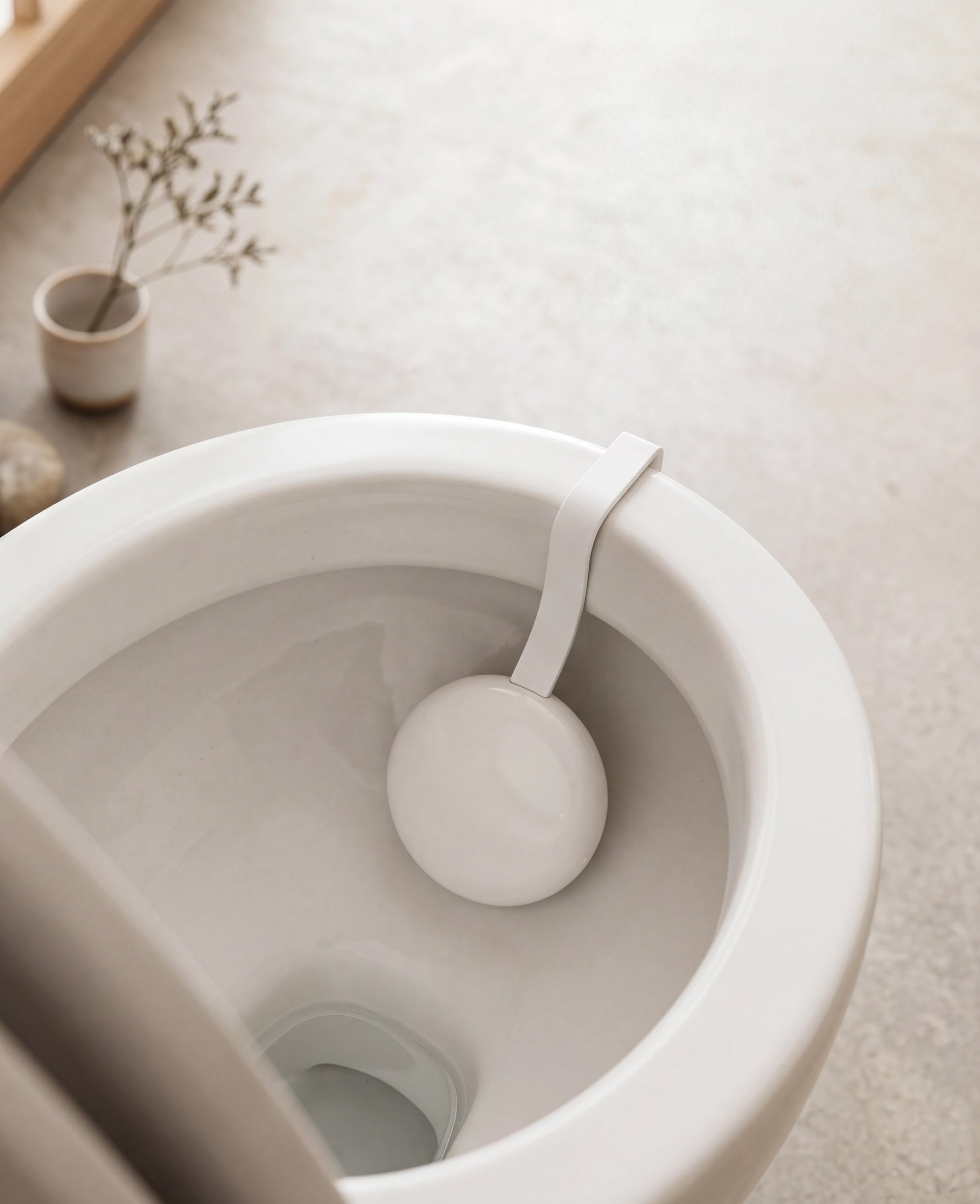 U-Scan Calci — Calci variant — Top-down view of the device clipped under a toilet bowl rim, beige tone, soft natural light, minimal bathroom setting — top-down, bathroom, minimal, beige