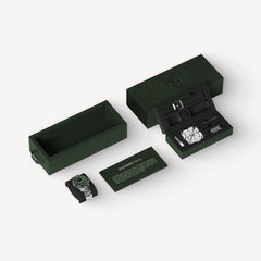 ScanWatch Nova — Verde 42mm — Unboxing completo: caja verde oscura abierta con reloj, correa, accesorios y tarjeta del producto sobre fondo gris claro — embalaje, unboxing, vista isométrica, caja verde