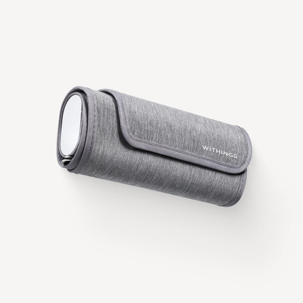 Withings BPM Connect — Verbundene Blutdruckmanschette — Dreiviertelansicht auf weißem Hintergrund, aufgerollte Manschette mit ovalem Silberdisplay und Withings-Logo — grau, kompakt, Stoff