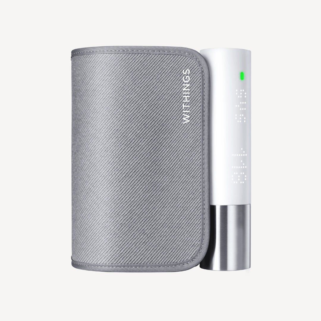 Withings BPM Core — Tensiomètre connecté — Vue de face sur fond blanc, brassard gris replié avec module blanc et base argentée, LED verte allumée — packshot, fond neutre, brassard, module